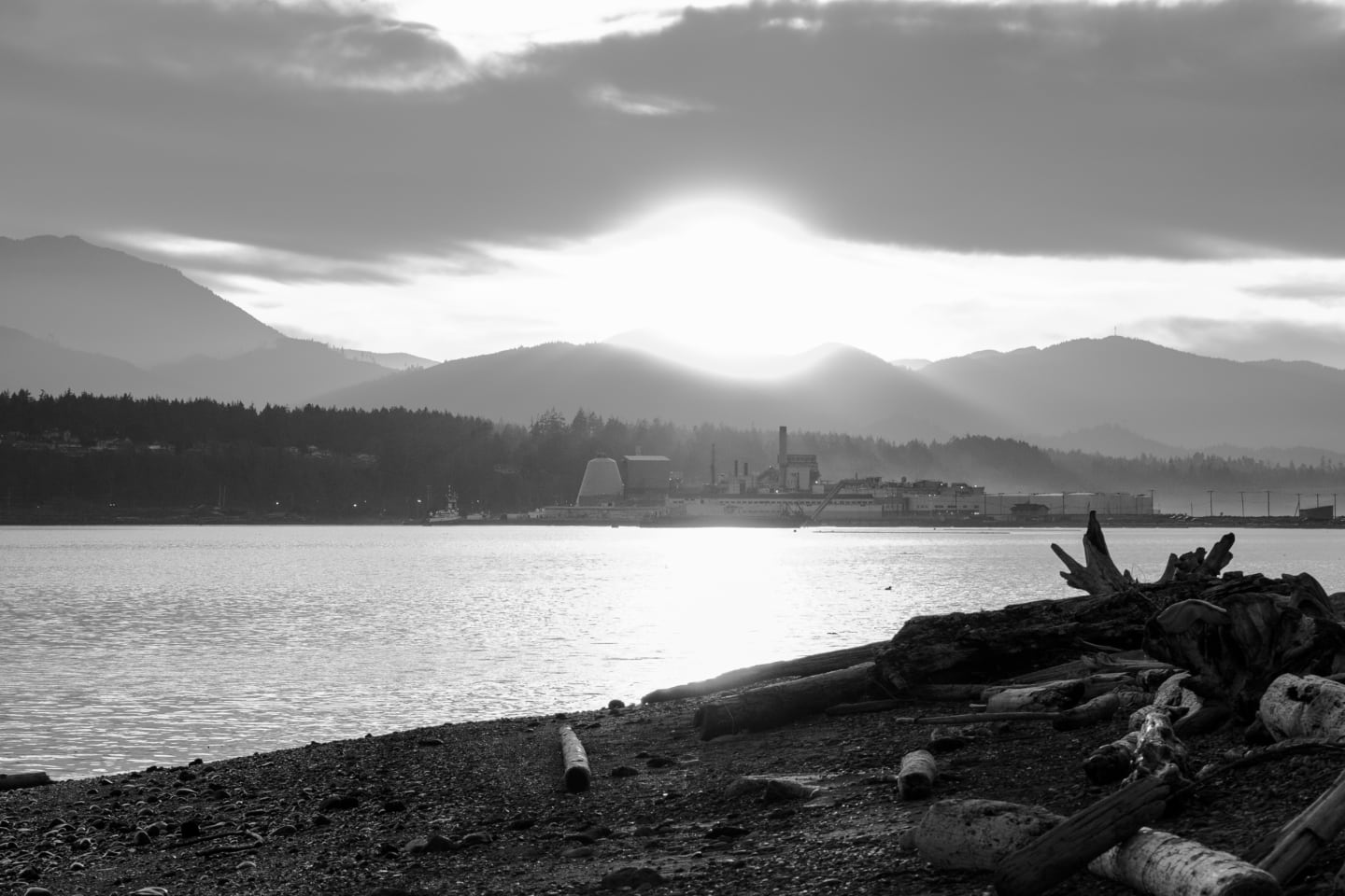 Dramatic black and white view of mill complex from waterfront at sunset