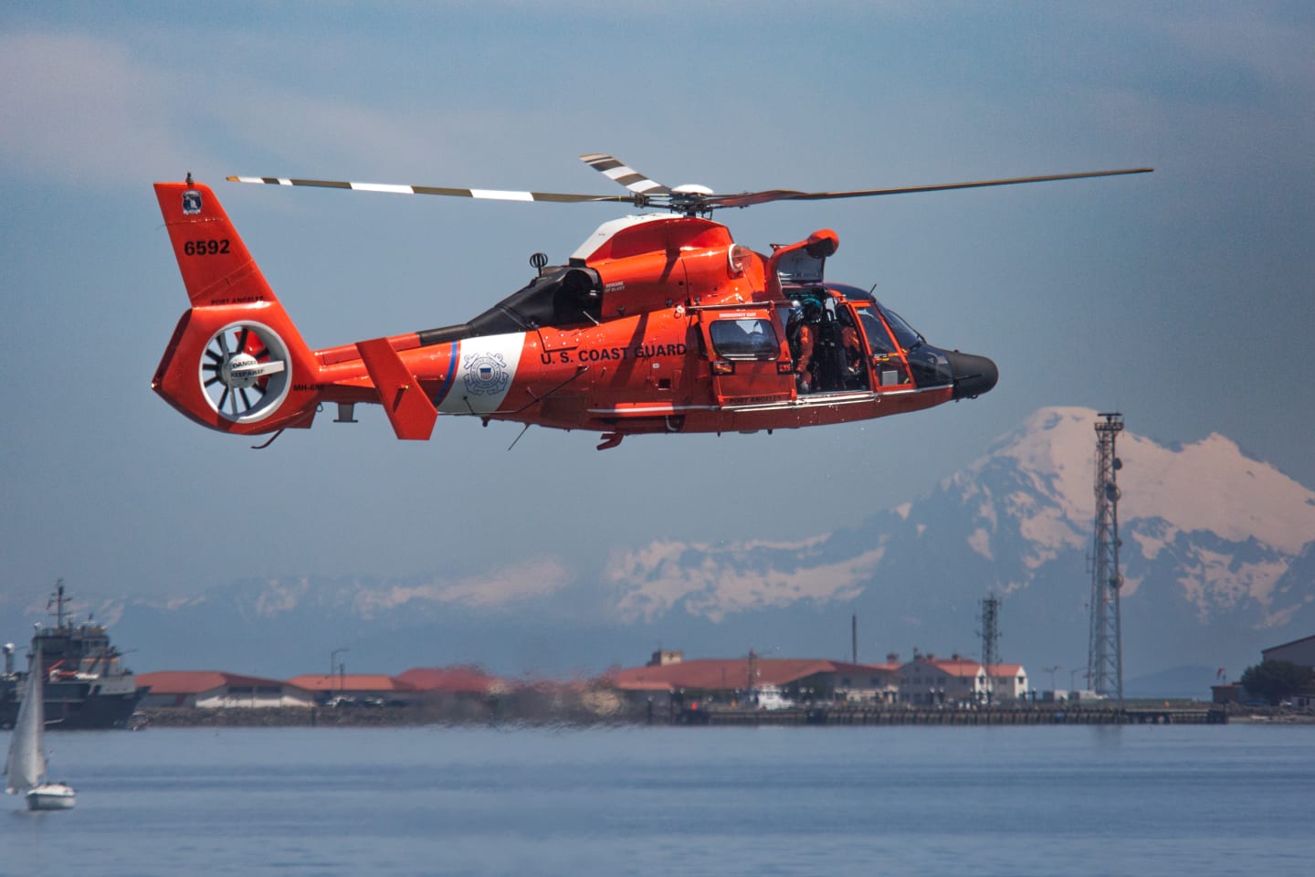 US Coast Guard helicopter flying over Port Angeles harbor with snow-capped Mount Baker visible across the strait