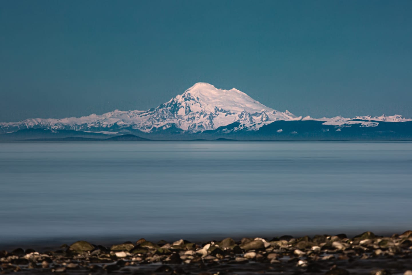 Mount Baker bathed in soft pink alpenglow light across the darkening waters of the strait