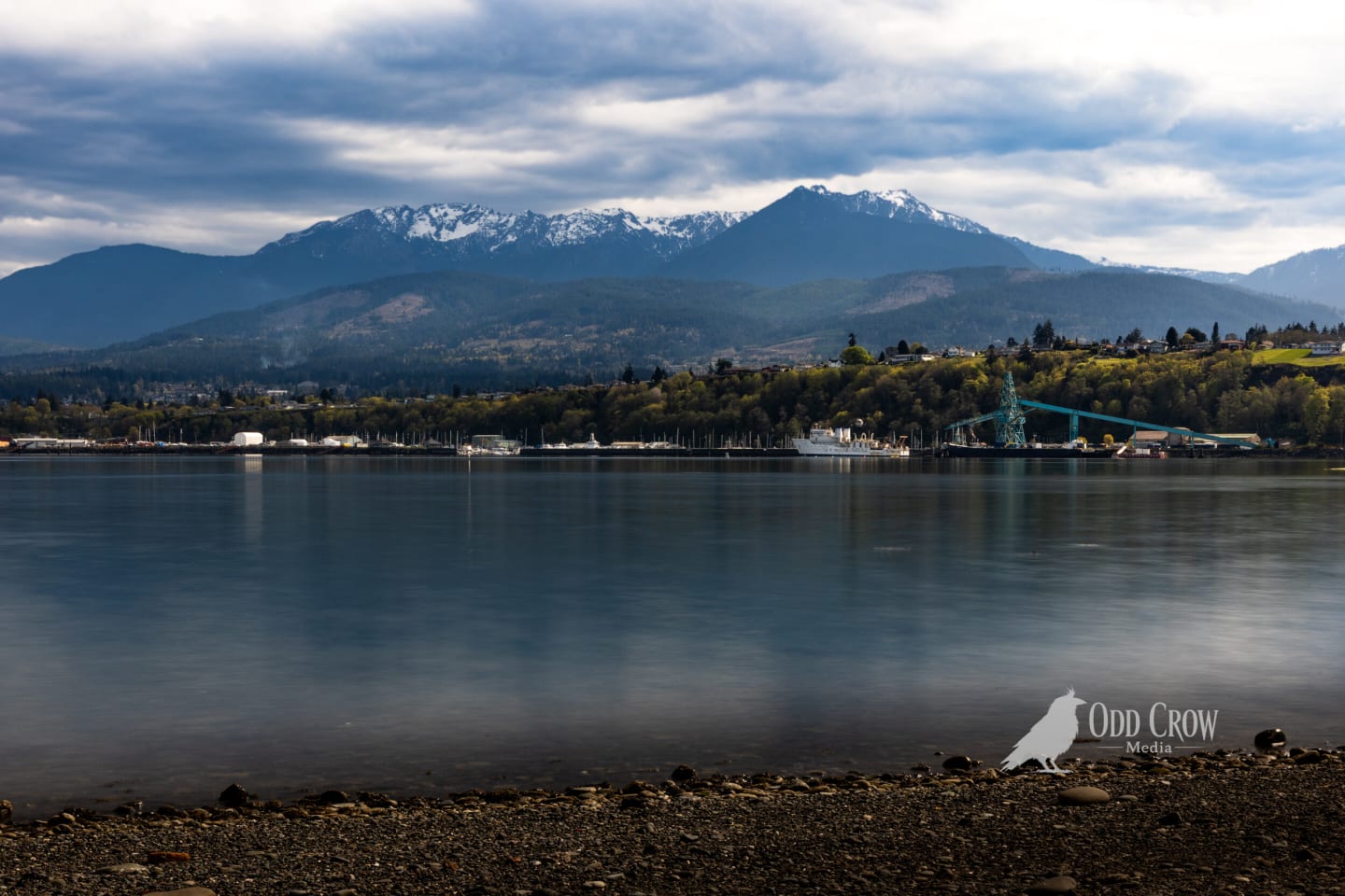 Calm harbor water reflecting cloudy sky with Port Angeles marina and Olympic Mountains in the distance