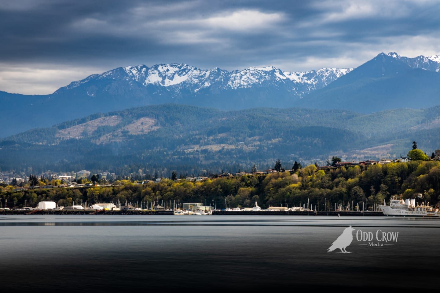 Wide view of Port Angeles Harbor with smooth water created by long exposure, showcasing marina and Olympic Mountain backdrop
