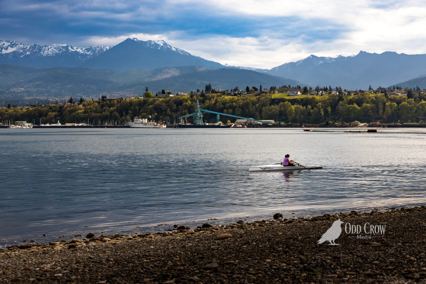 Single sculler on glass-smooth harbor water with dramatic layered mountain backdrop and atmospheric lighting