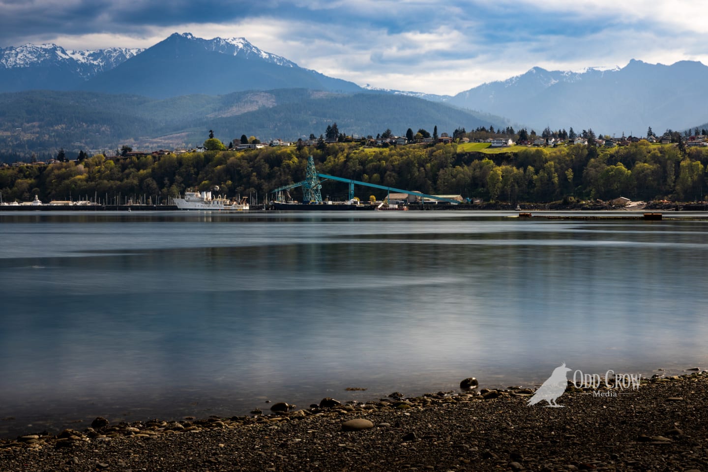 Serene harbor view with ultra-smooth water and snow-covered Olympic Mountains under dramatic cloudy sky