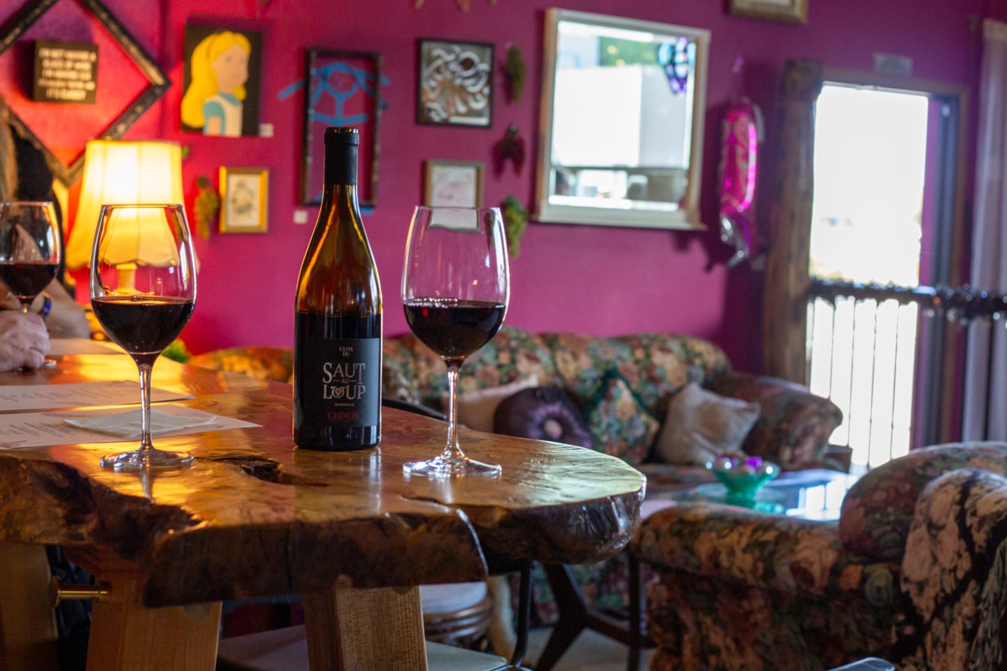 Wine glass and bottle of red wine on rustic wooden table in cozy interior setting with warm lamp lighting