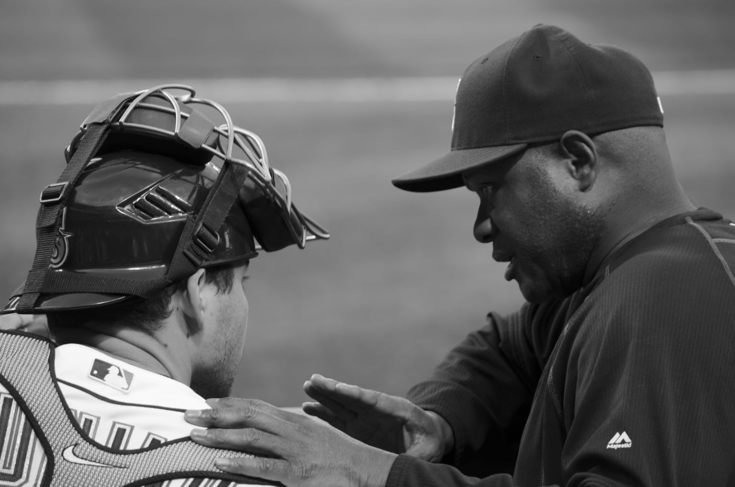 Black and white image of catcher and coach in close conversation during the game