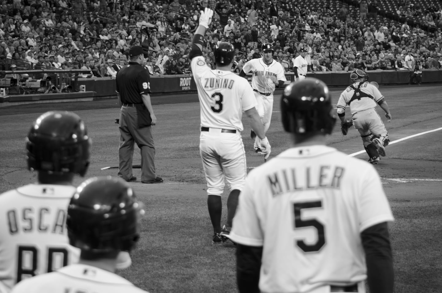 Black and white celebration scene showing Zunino crossing home plate with teammates