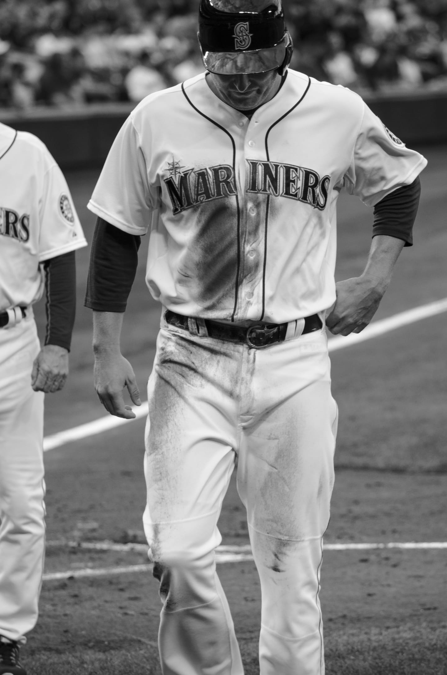 Black and white photo of a Mariners player walking in uniform, head down in concentration
