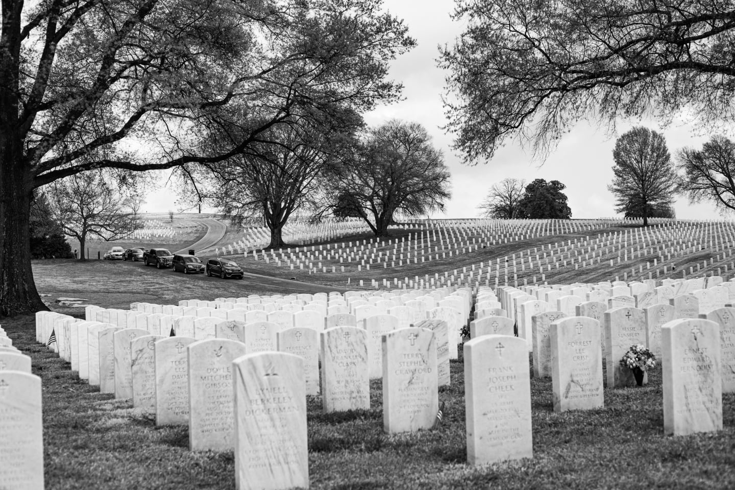 Wide view of Arlington Cemetery with rows of white headstones stretching across rolling hills with bare trees