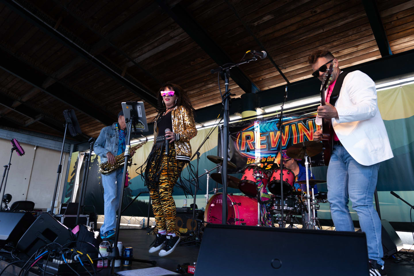 Rewind band performing on stage at Concerts on the Pier Port Angeles - lead singer in gold sequin jacket and tiger print pants mid-dance, saxophonist and guitarist in background