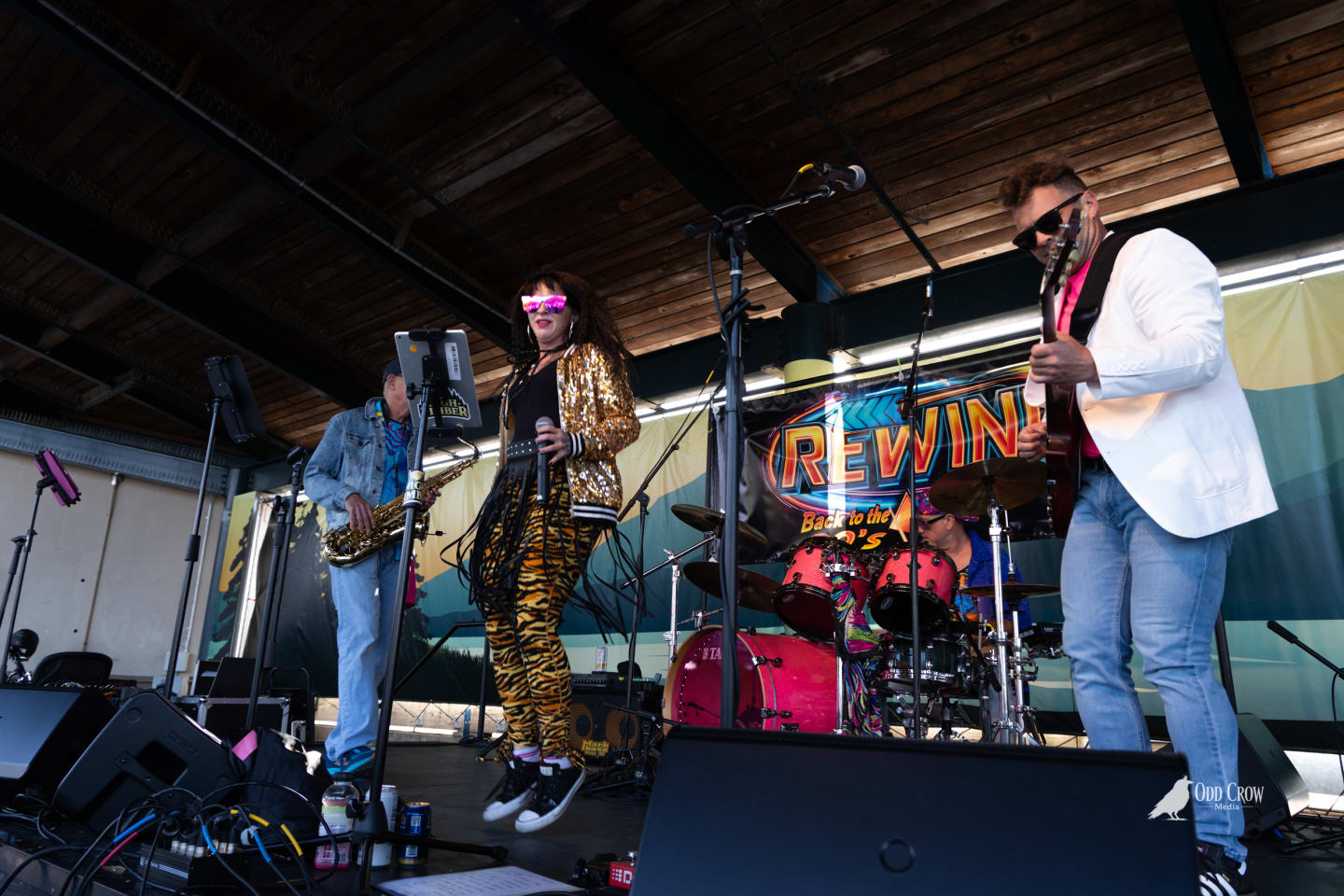 Rewind band performing on stage at Concerts on the Pier Port Angeles - lead singer in gold sequin jacket and tiger print pants mid-dance, saxophonist and guitarist in background