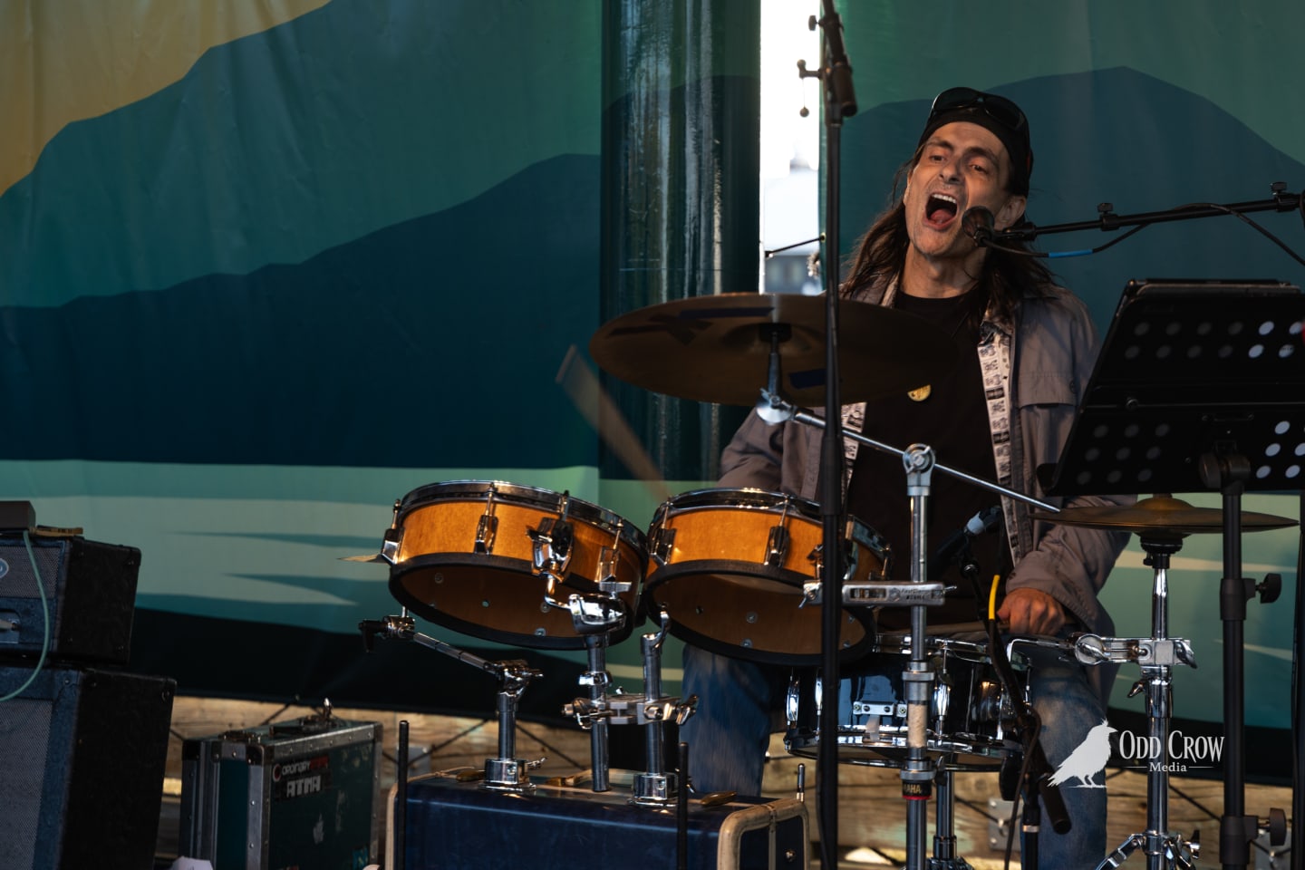 Foot Stompers drummer mid-song, mouth open wide singing into a mic while playing twin snare drums, energy visibly high on stage