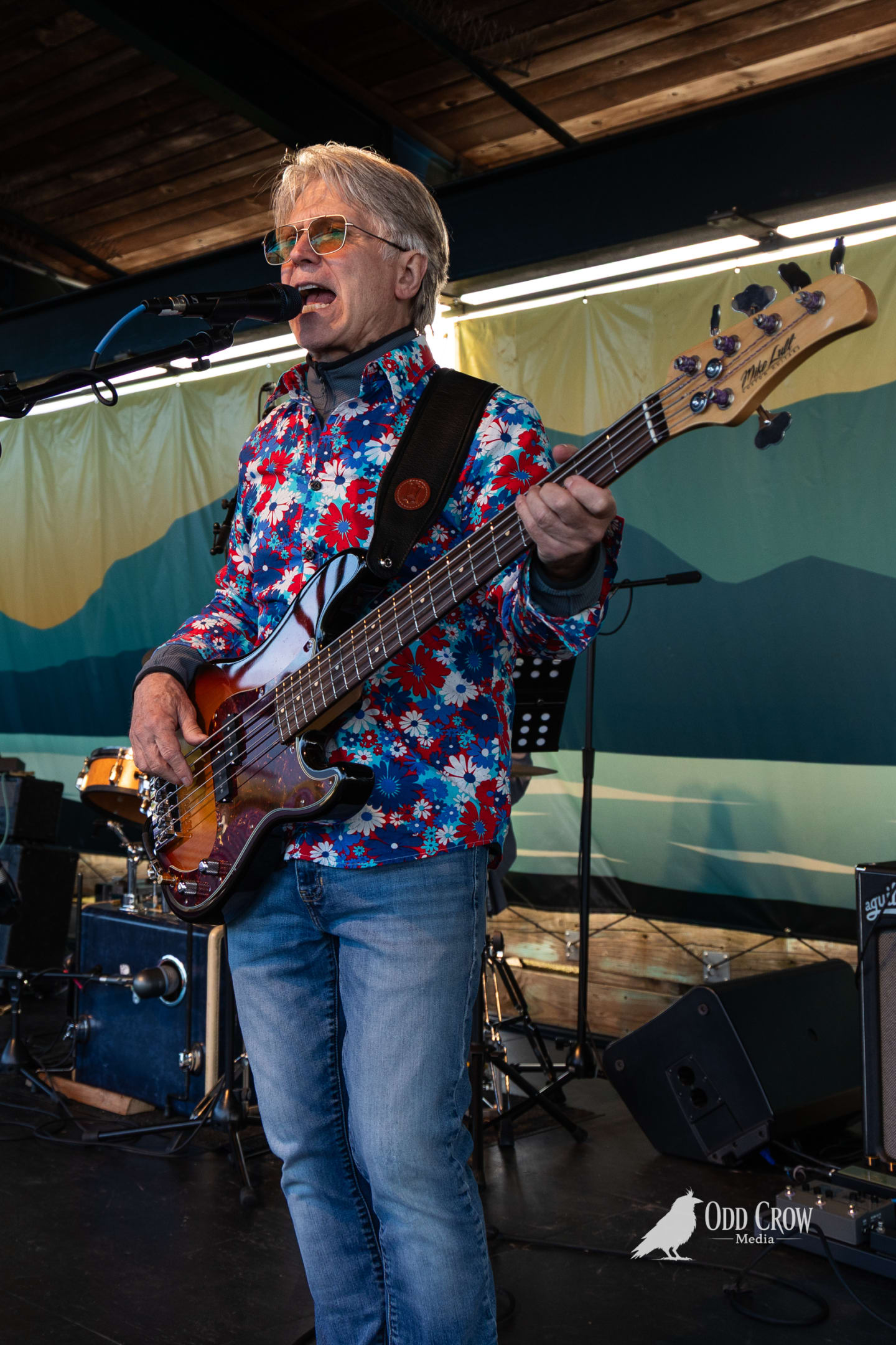 Foot Stompers bassist performing in a bold red, white, and blue floral shirt, playing a five-string bass and singing at Concerts on the Pier