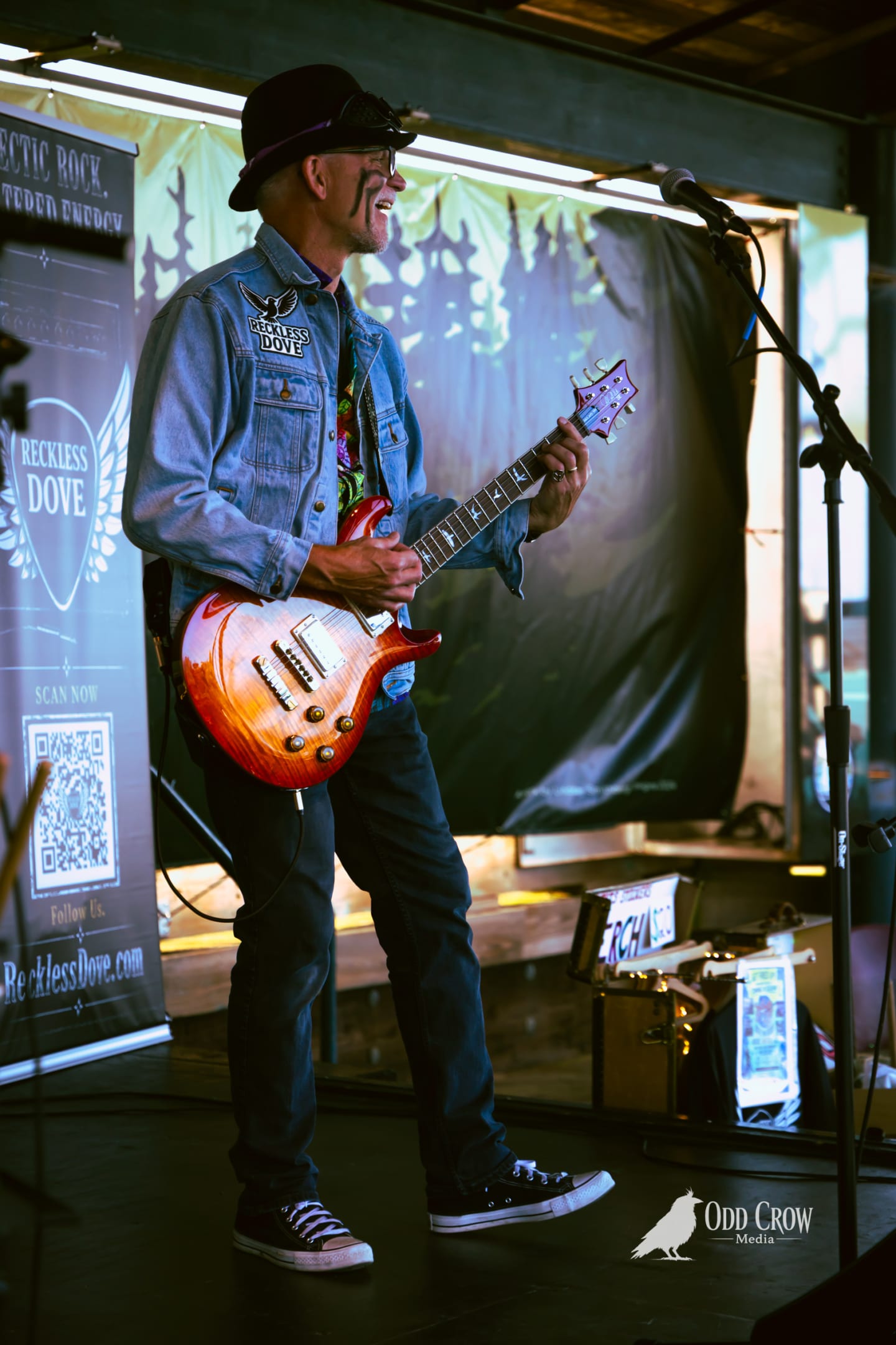 Reckless Dove guitarist in a denim jacket, laughing mid-song on the Port Angeles pier stage