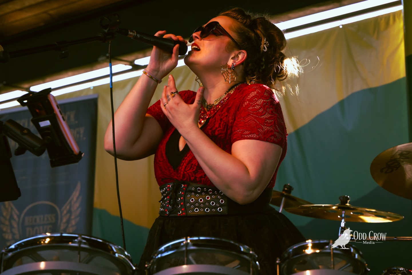 Bee Smith singing next to the drum kit, backlit by string lights on the pier