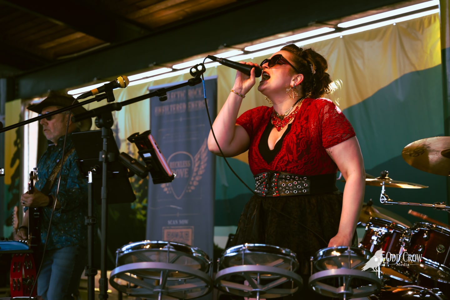 Bee Smith of Reckless Dove singing with one arm raised overhead, red lace top and studded belt, on the Port Angeles pier stage