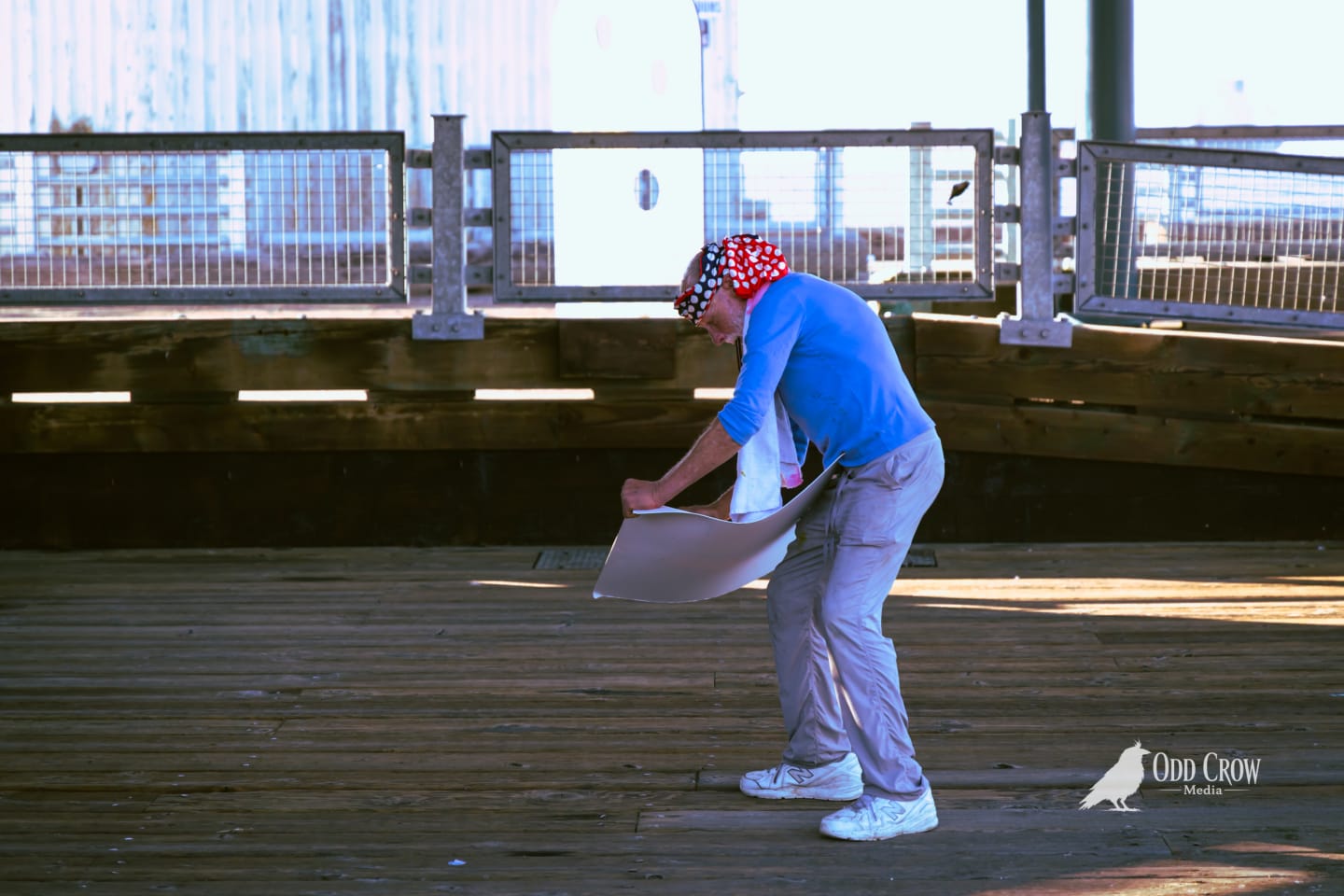 The same street artist working on his sketch, pier railing and water in the background