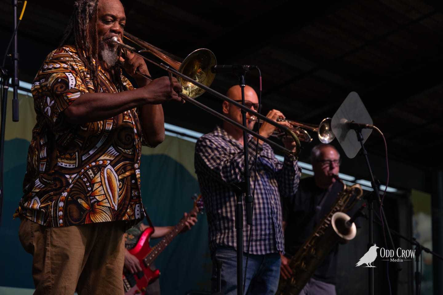 Ska band horn section performs trombone and trumpet on an outdoor stage at a waterfront pier festival.