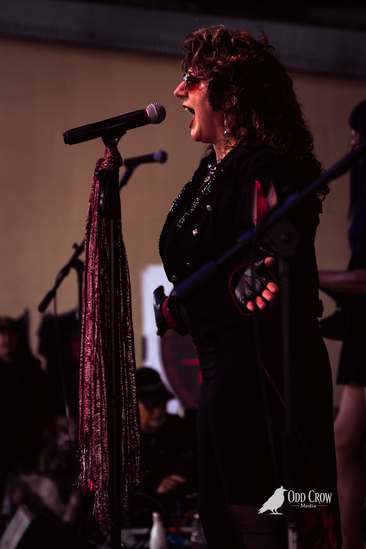 Female vocalist in black performing passionately at outdoor pier concert, microphone stand adorned with red metallic fringe.