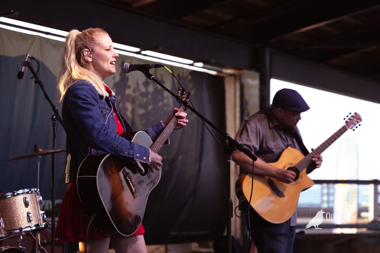 Blonde female guitarist performs at an outdoor pier stage alongside a male guitarist.