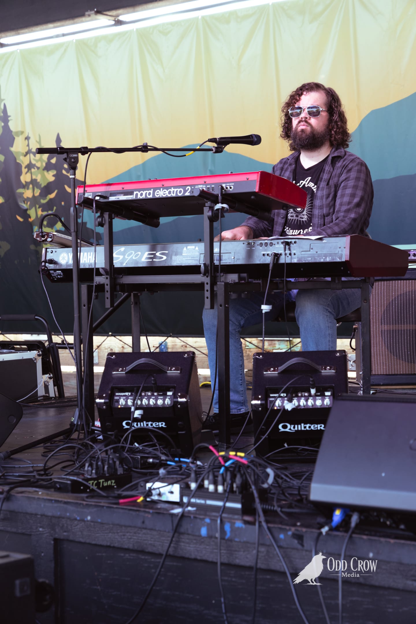 Bearded keyboardist plays Nord Electro 2 and Yamaha S90ES on an outdoor festival stage.