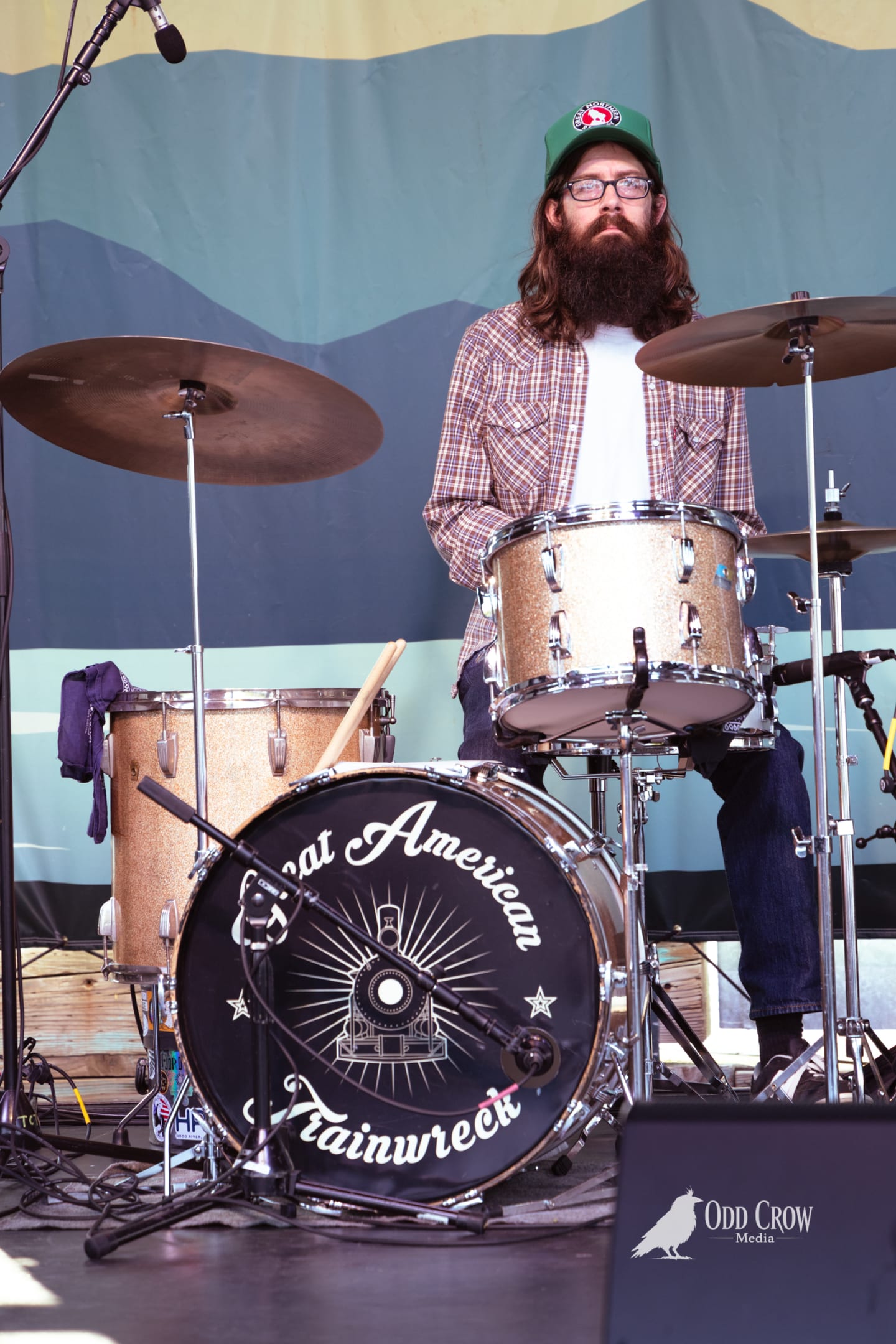 Bearded drummer performing live on stage behind a Great American Trainwreck bass drum kit.
