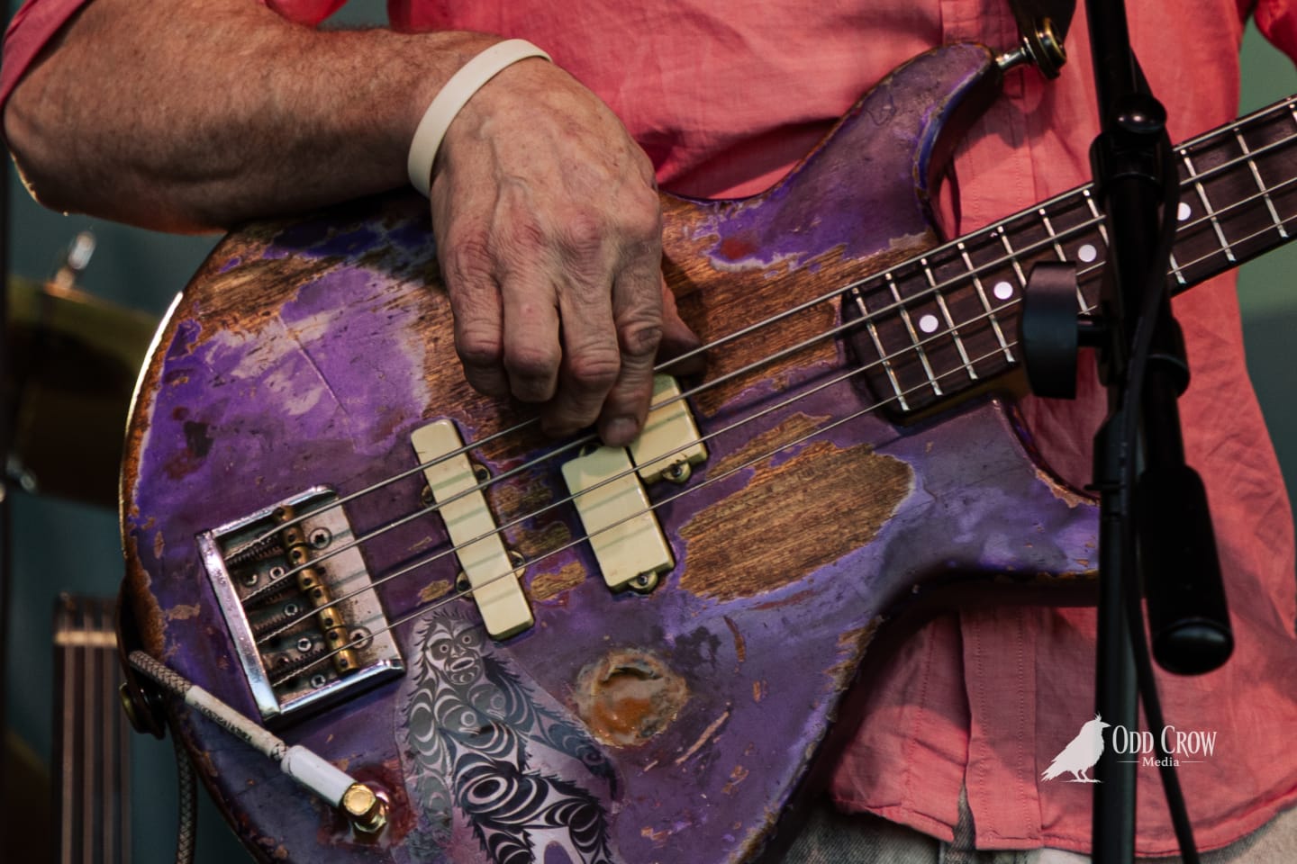 Weathered purple bass guitar being played by an older musician wearing a white wristband.