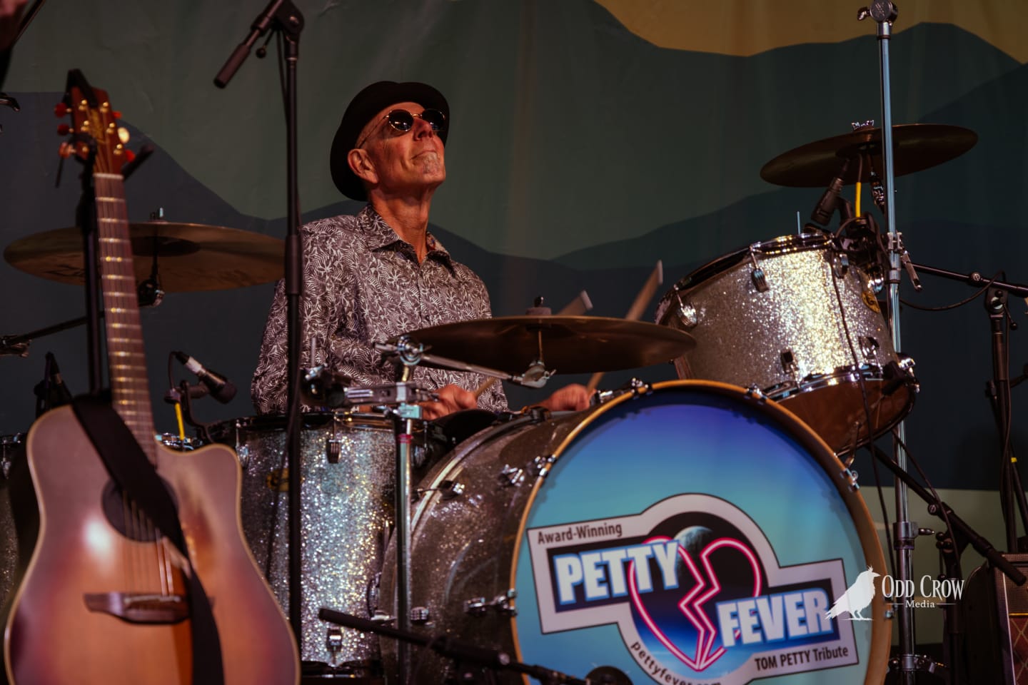 Petty Fever drummer in patterned shirt and black fedora plays sparkle kit, with the Petty Fever Tom Petty Tribute bass drum head visible in the foreground
