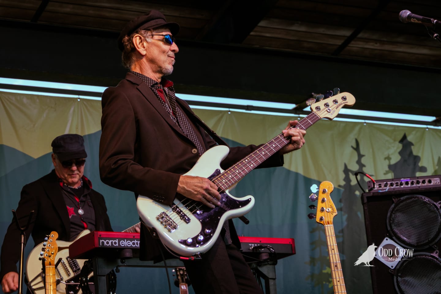 Petty Fever front man in red shirt singing into mic and playing Rickenbacker guitar, pointing upward with energy, two bandmates behind him