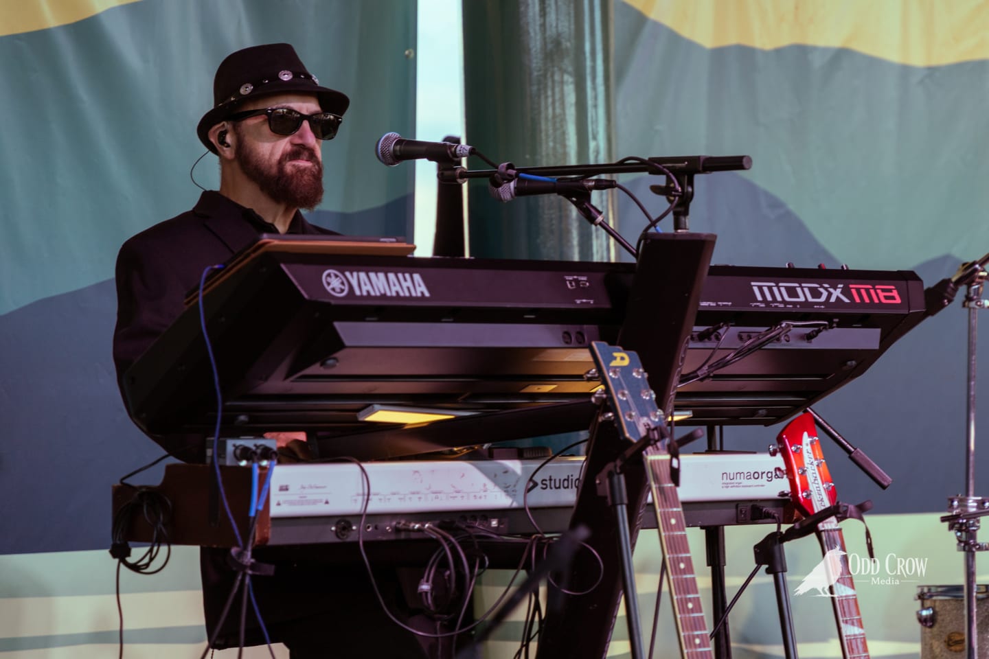 Petty Fever guitarist in black hat playing blue Duesenberg guitar and singing, another guitarist visible in the background