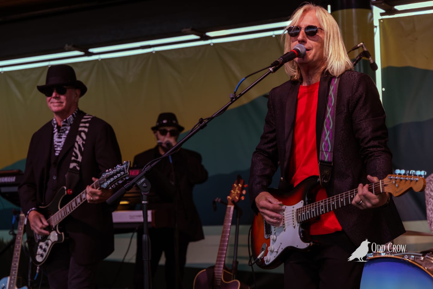 Petty Fever guitarist playing blue Duesenberg guitar, focused on fretwork, Petty Fever bass drum visible in the lower right