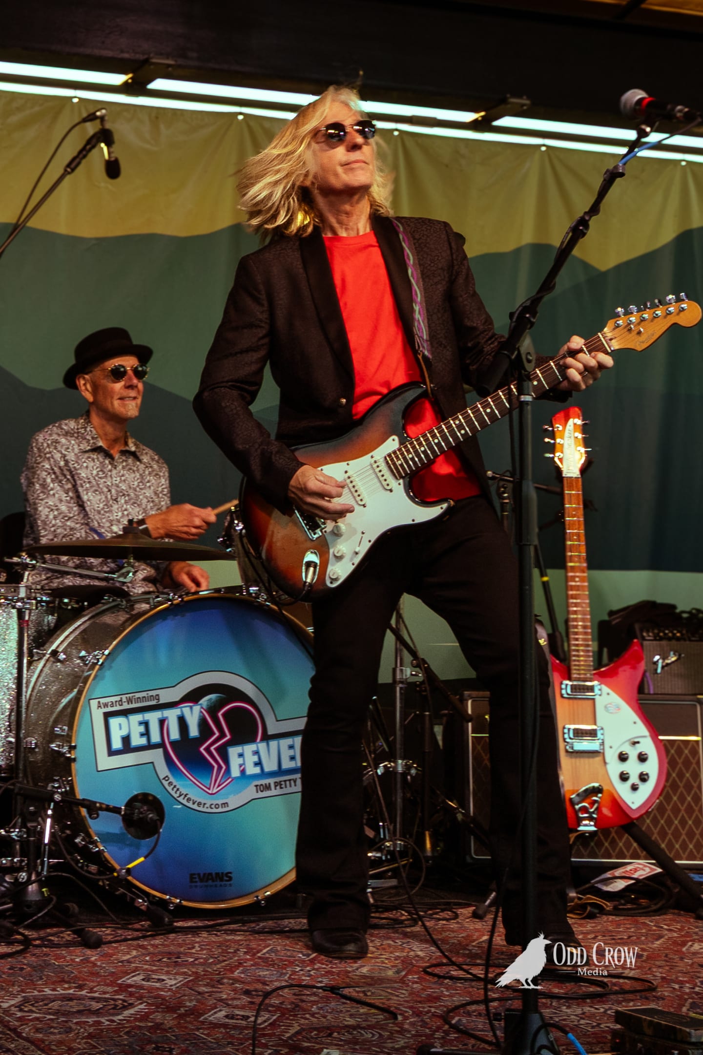 Petty Fever bassist in black cap smiling at the camera between songs, stage lights catching the neck of his white bass guitar
