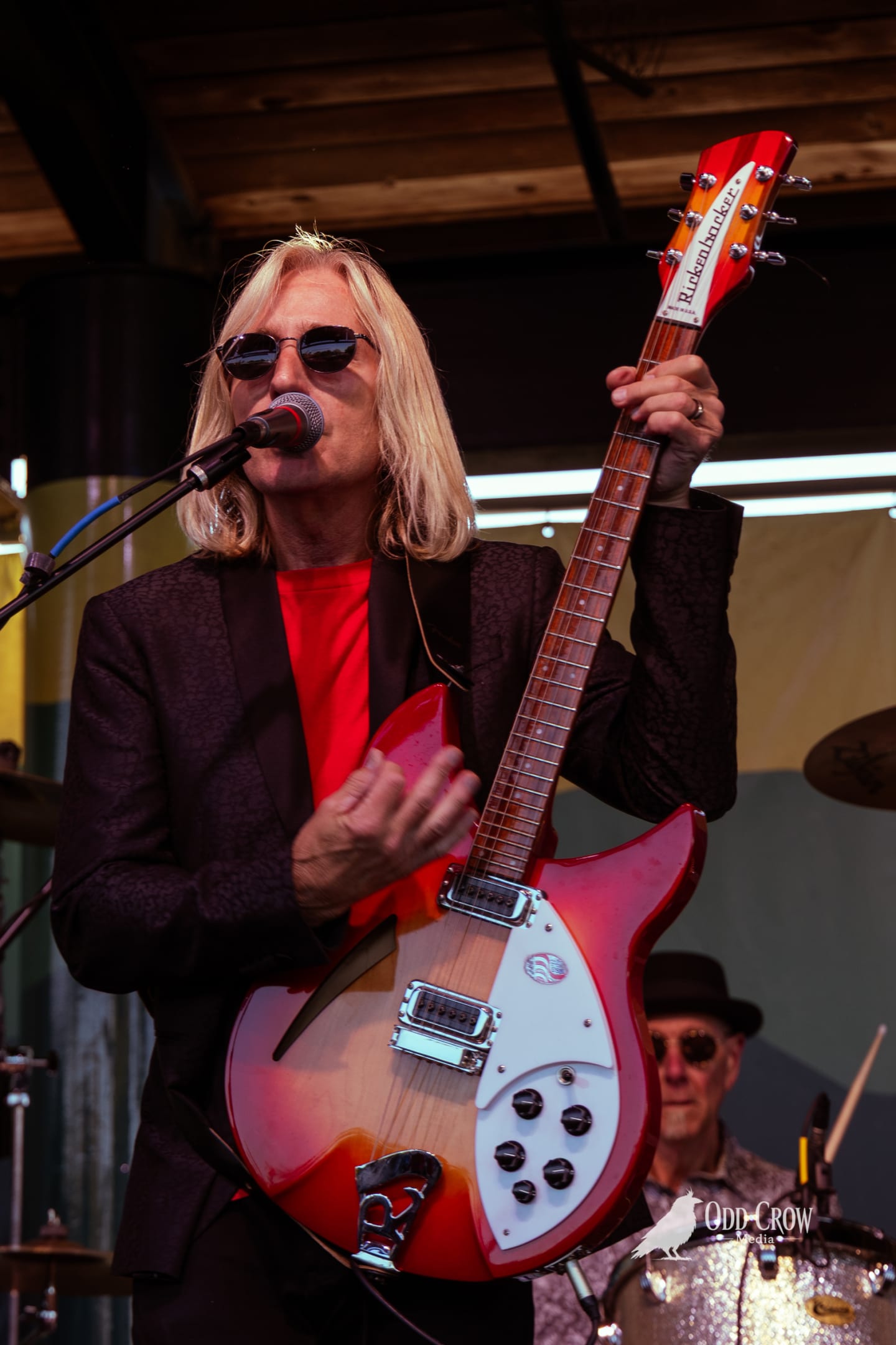 Petty Fever front man in top hat and red shirt singing into the mic with Rickenbacker guitar, warm stage lights glowing behind him