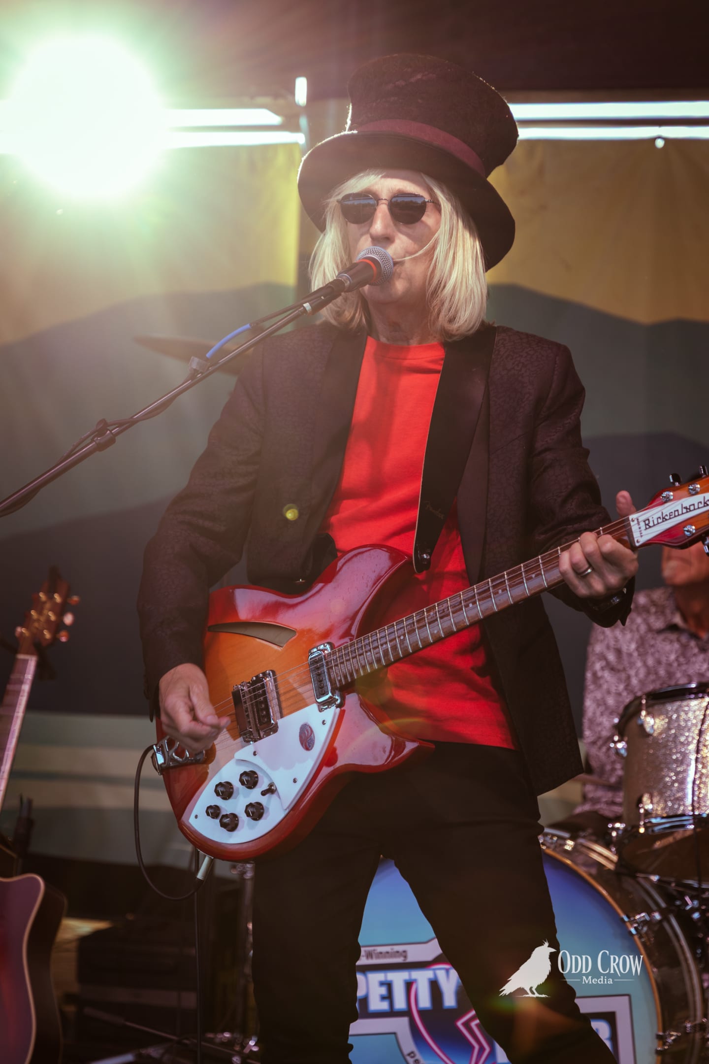 Petty Fever band full stage shot from side angle, singer in top hat and red shirt center, crowd visible on the Port Angeles waterfront behind them