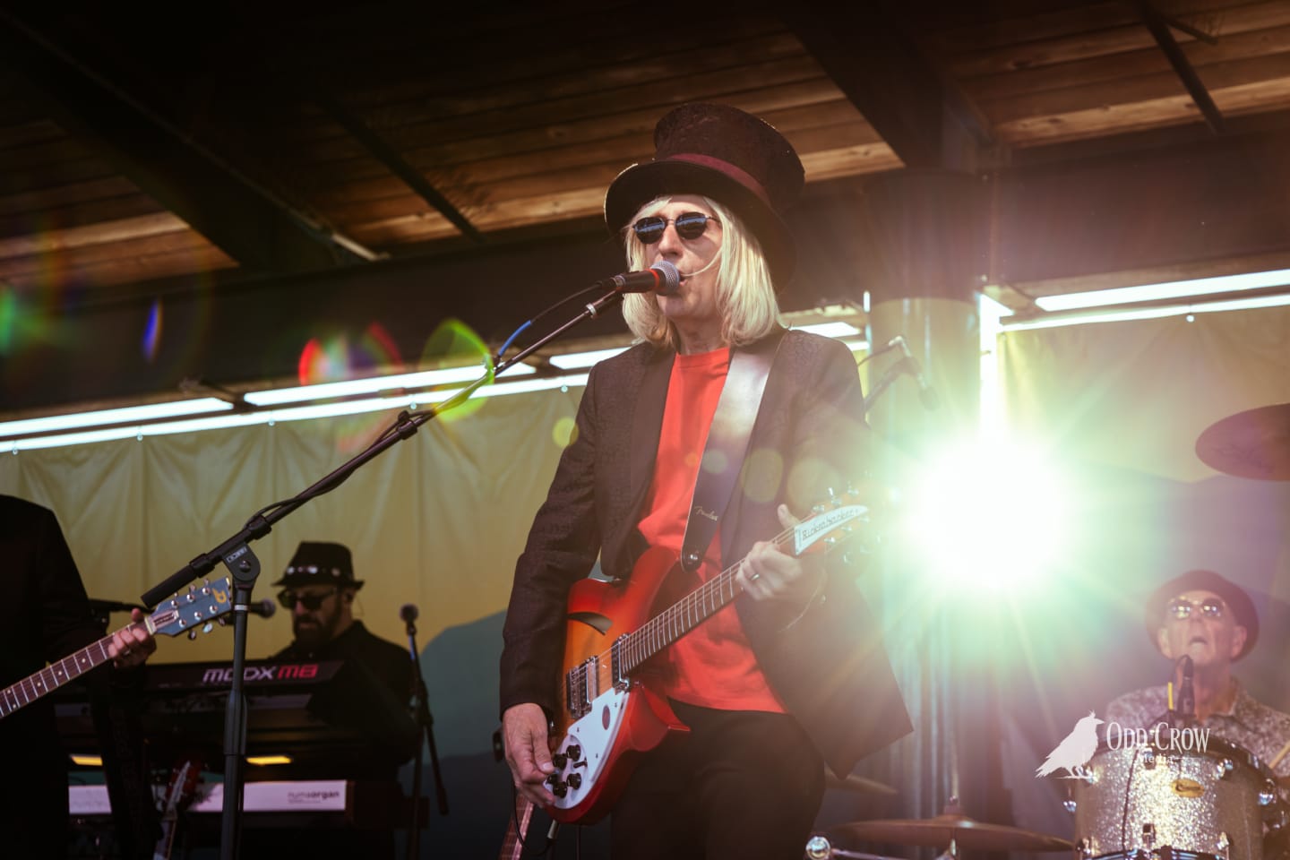 Petty Fever singer playing sunburst Rickenbacker guitar with front man energy, bass drum logo visible and Fender amp behind him