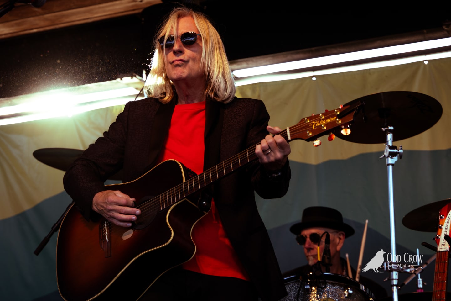 Petty Fever front man in red shirt and Stratocaster guitar flanked by guitarists, stage lights creating starburst effects, crowd behind the band