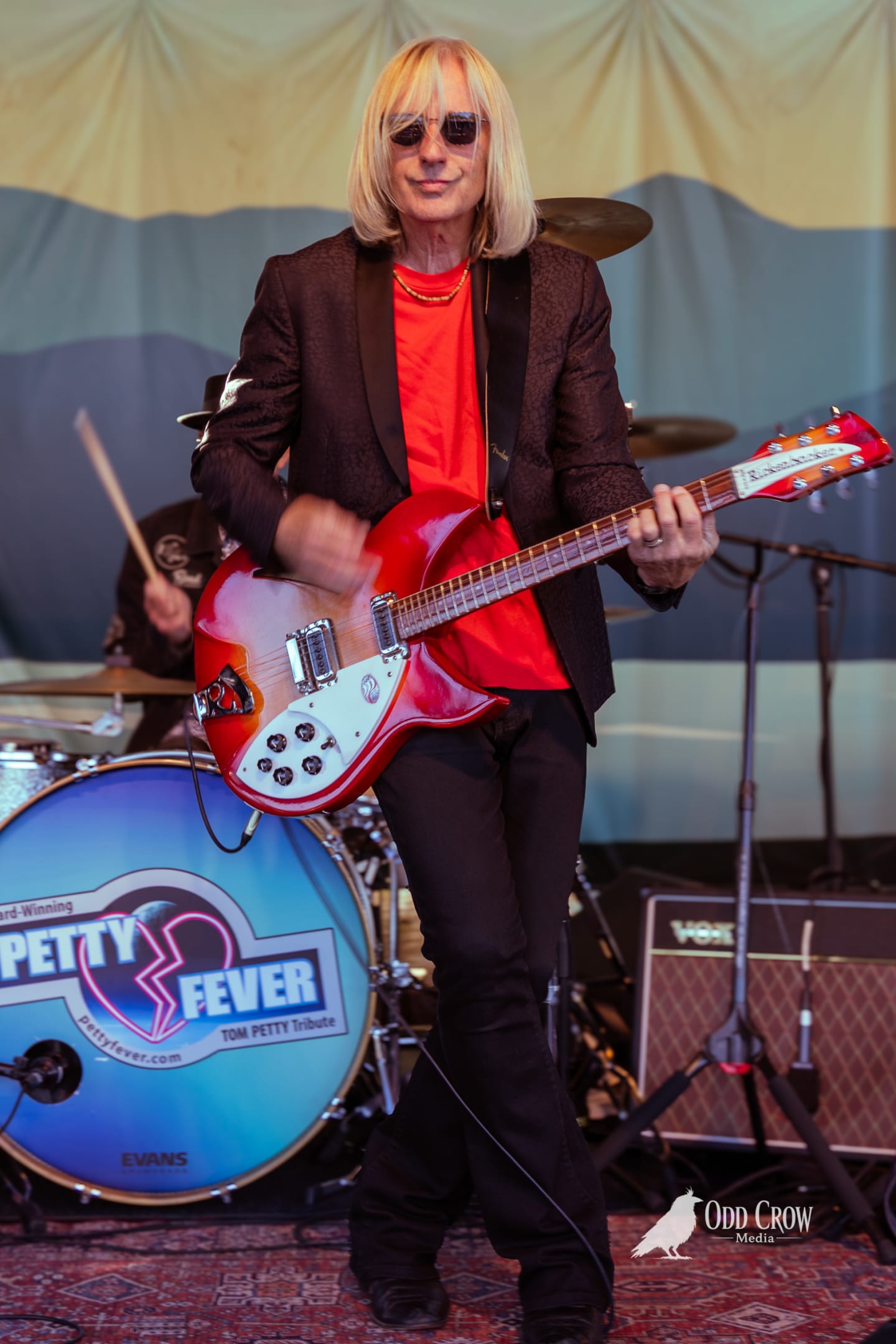 Petty Fever singer with arms wide open holding acoustic guitar, crowd visible, stage light warming the scene at Concerts on the Pier