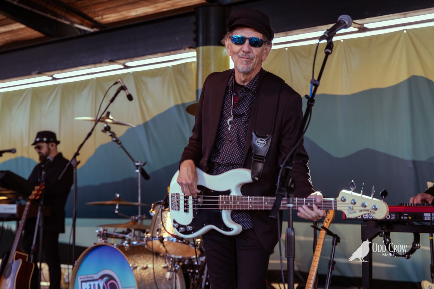 Petty Fever singer playing acoustic guitar on stage at Concerts on the Pier, wide-angle stage shot showing full band and open-air pavilion setting