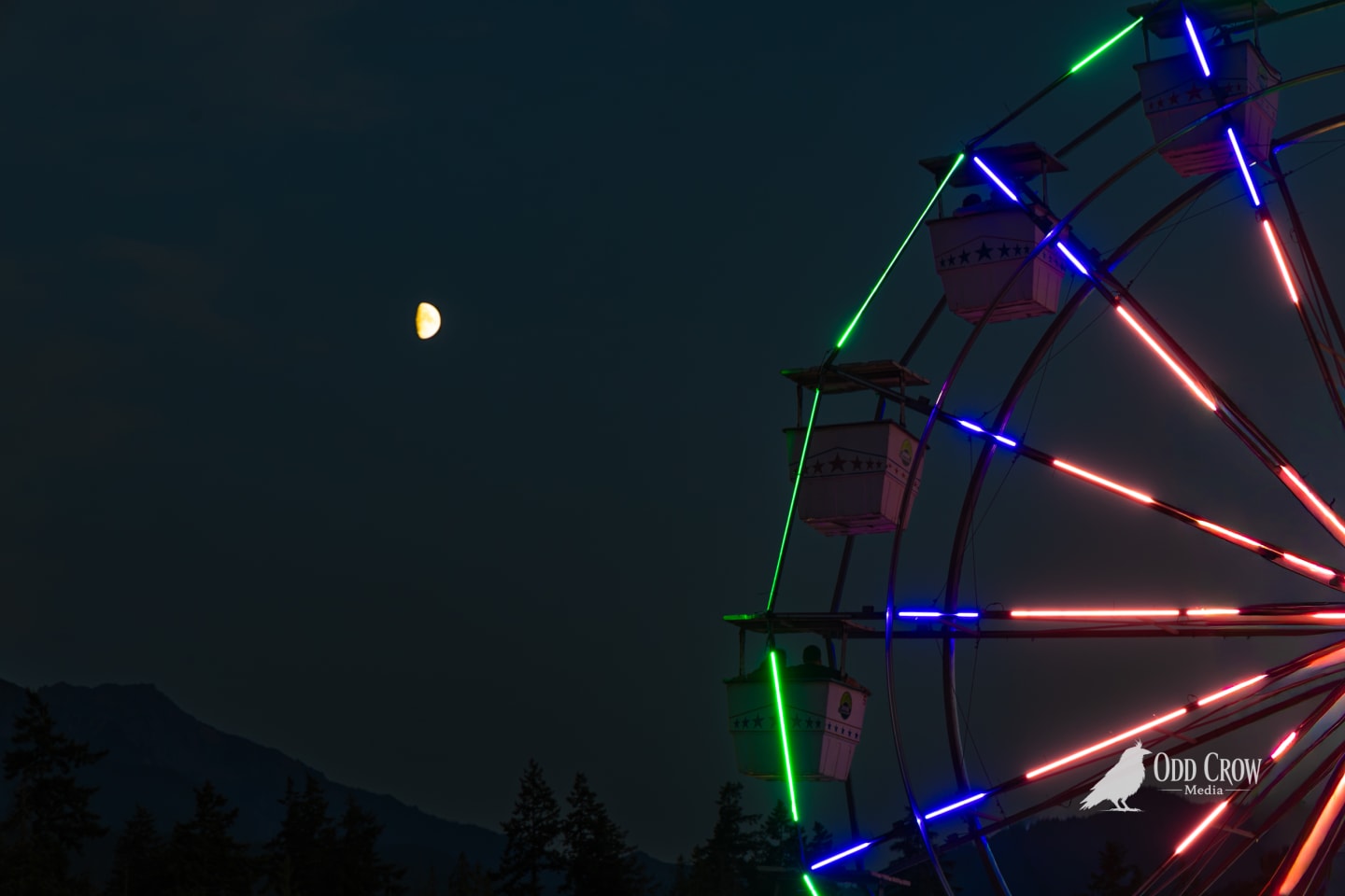 Clallam County Fair Ferris wheel with neon red, blue, and green spoke lights against a deep teal night sky, half moon glowing to the left