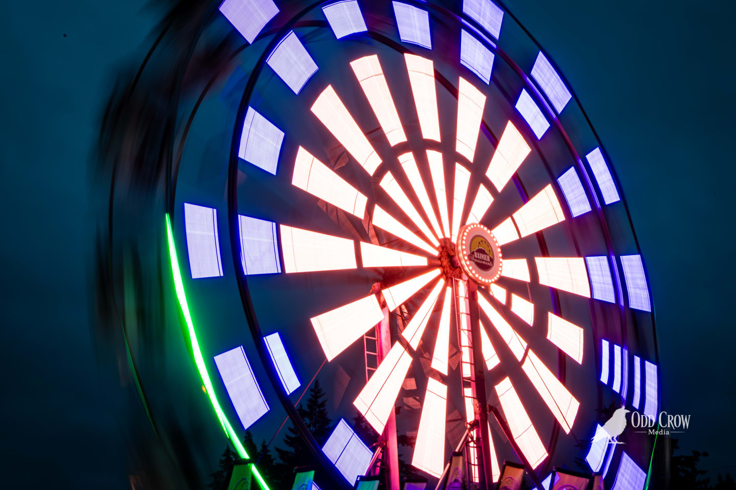 Close long-exposure shot of the Rainier Wheel Ferris wheel spinning at the Clallam County Fair, the lit panels creating a nearly solid disc of warm white and blue light