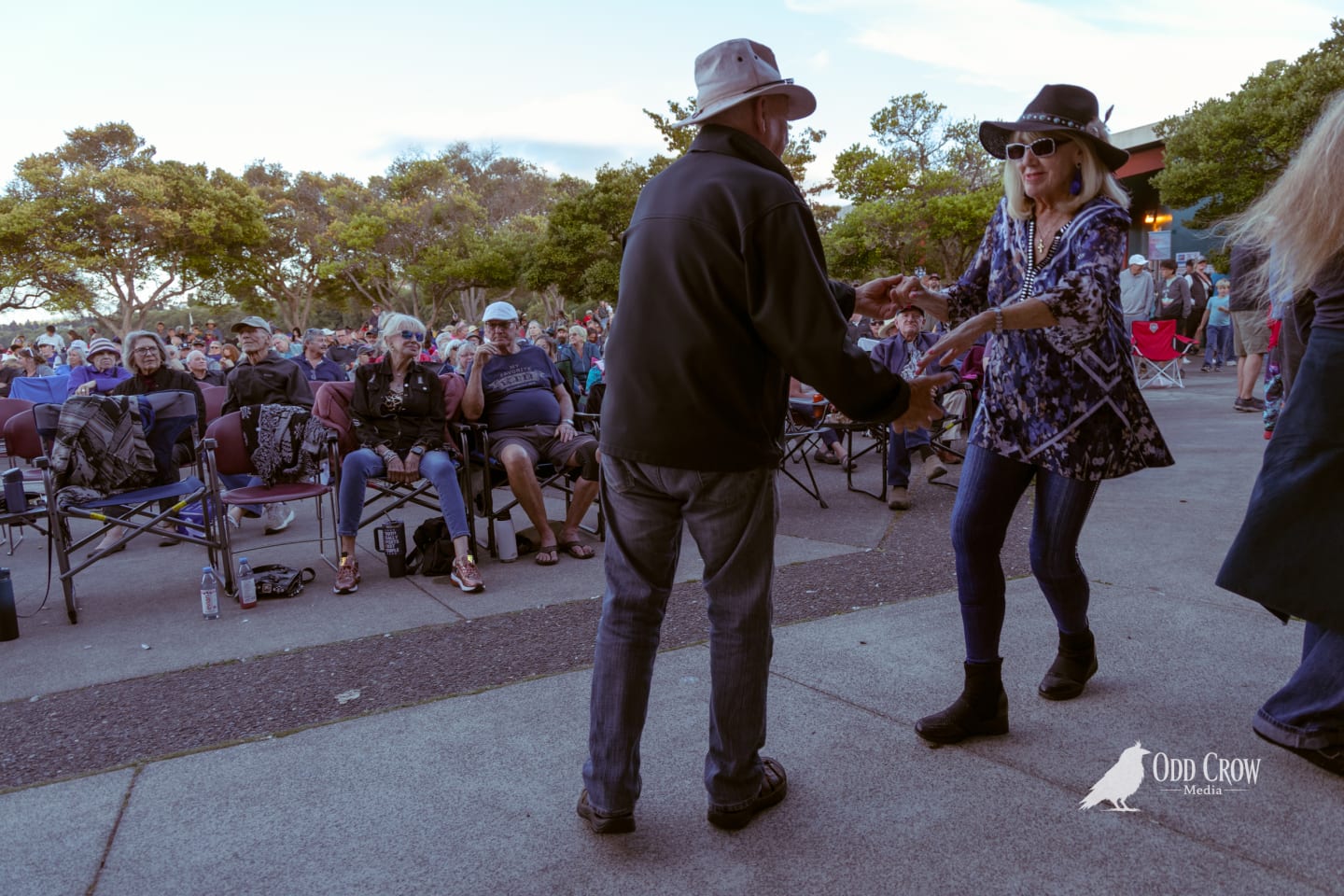 Couple dancing together at an outdoor evening concert with a large seated crowd behind them.