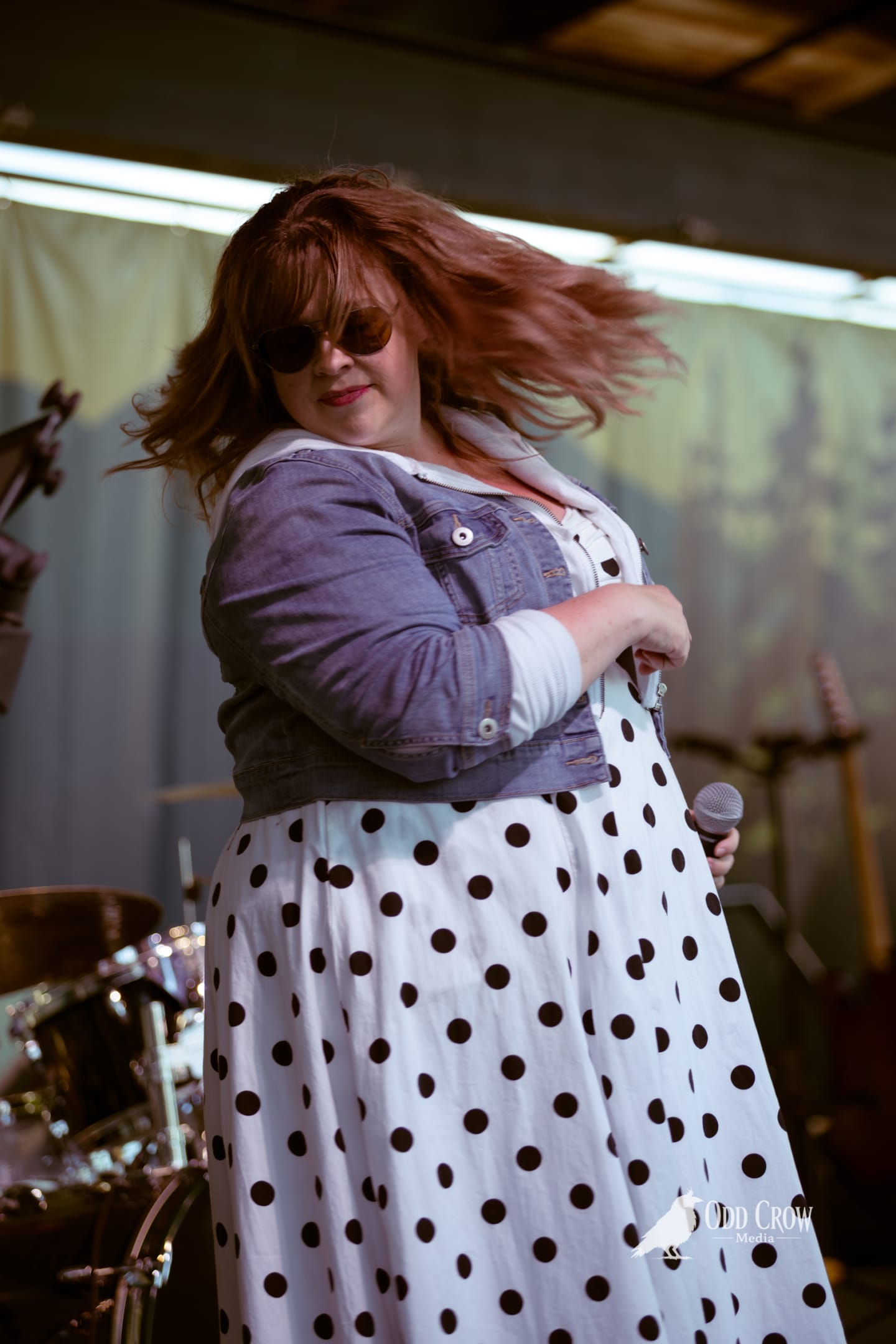 Female vocalist with flowing red hair performs on stage in polka dot dress and denim jacket.