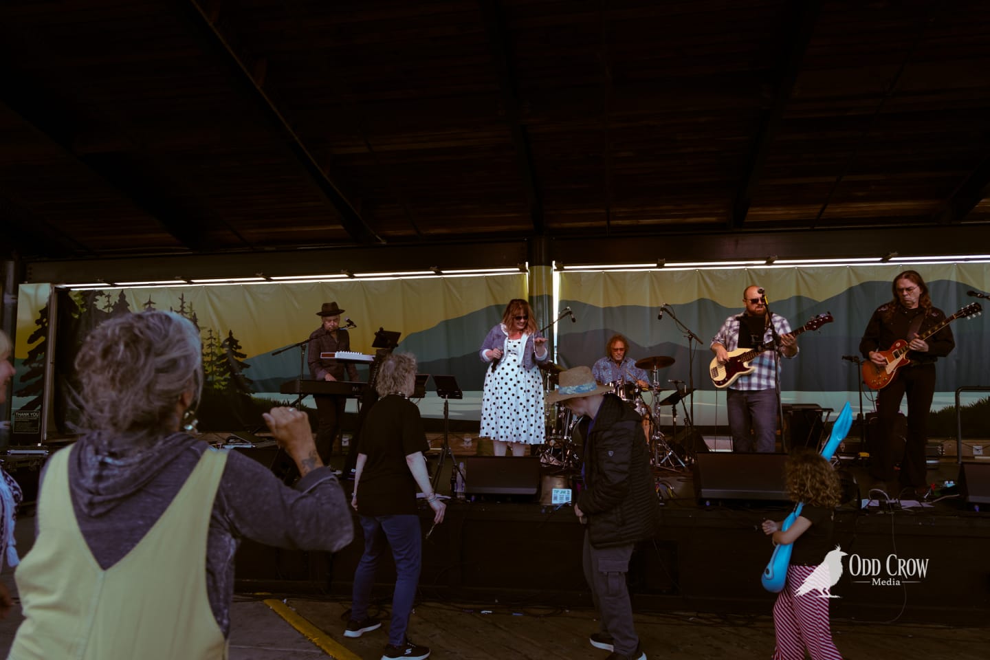 Band performs on outdoor stage while audience members dance in the foreground at a summer festival.
