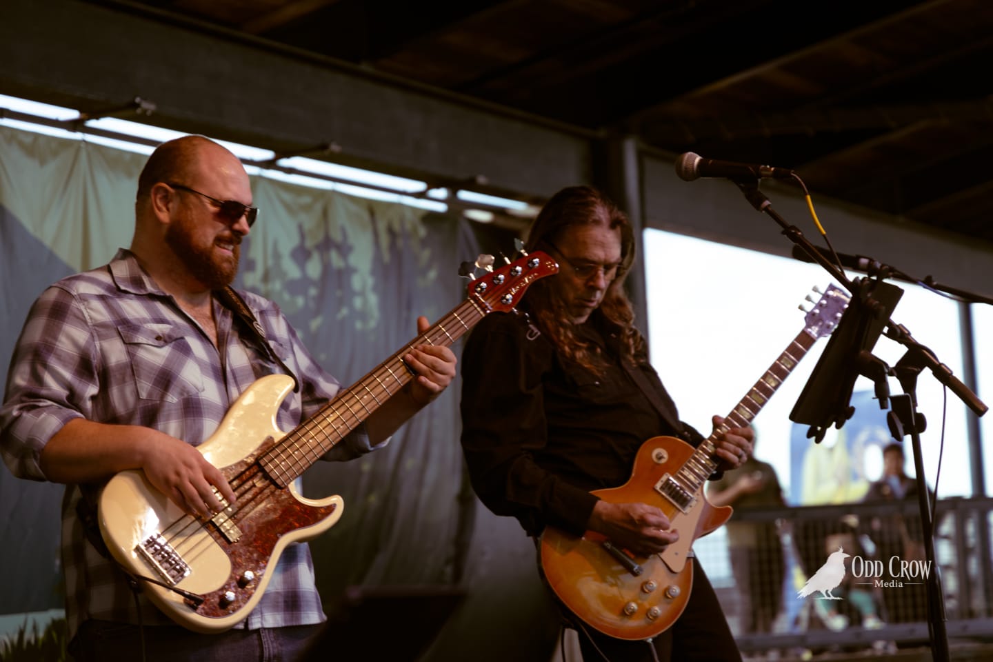 Two guitarists performing on a covered outdoor stage at a pier venue.