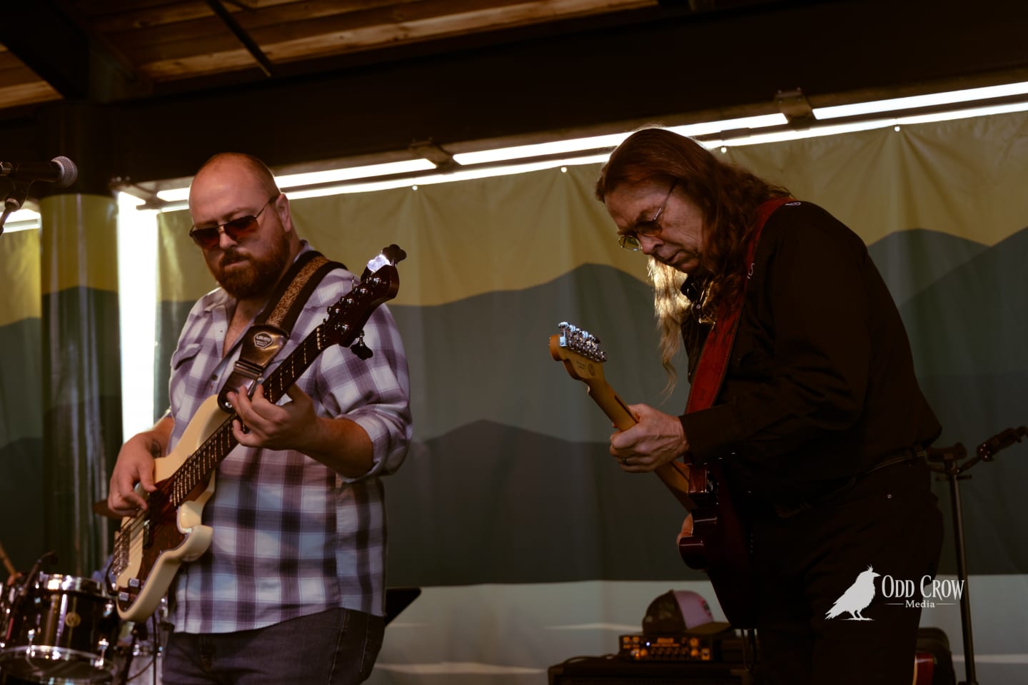 Two guitarists performing on stage at an outdoor pier venue, both focused on their instruments.