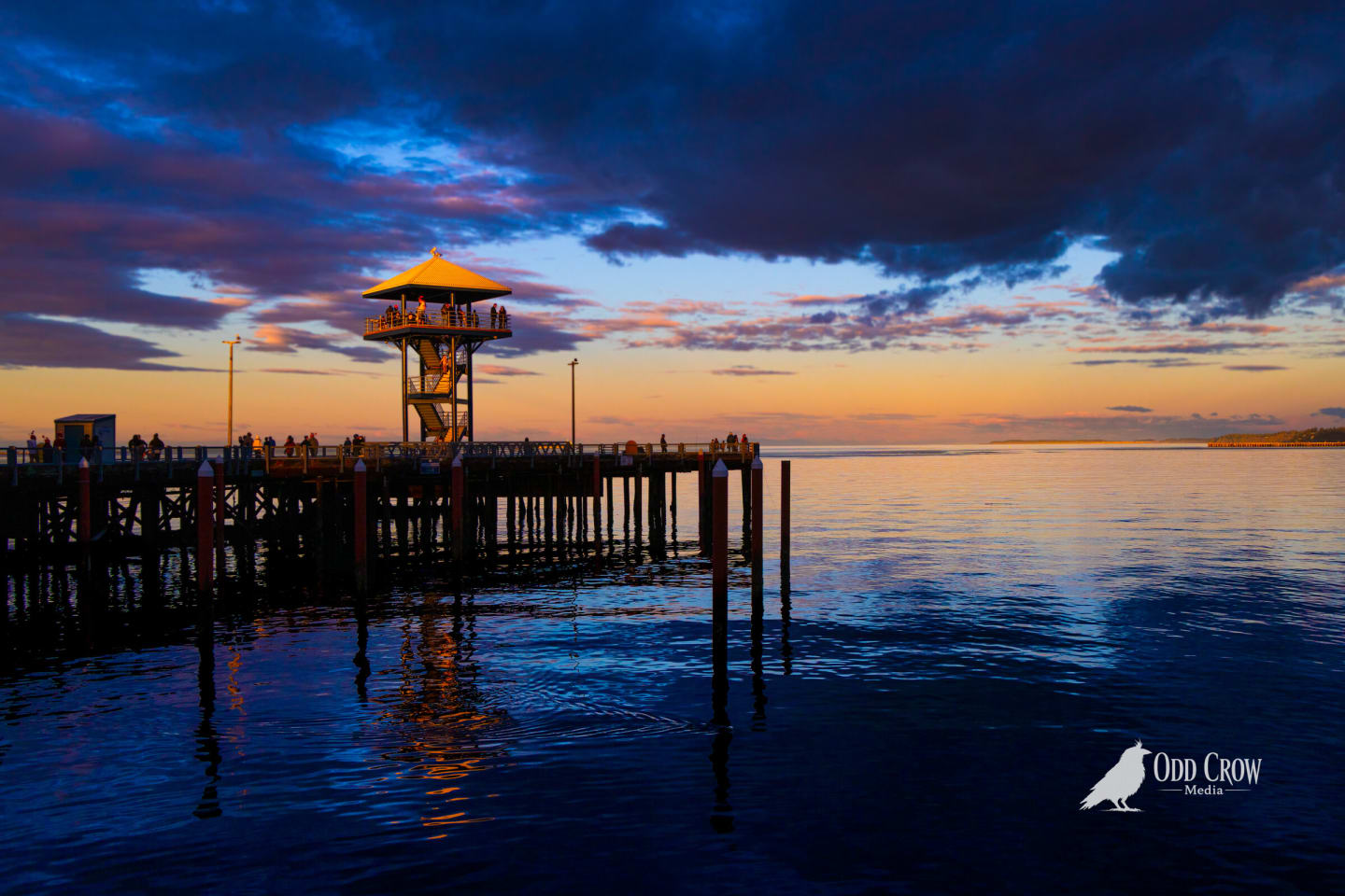 Port Angeles city pier at sunset, the observation tower lit gold against deep blue and orange clouds over the Strait