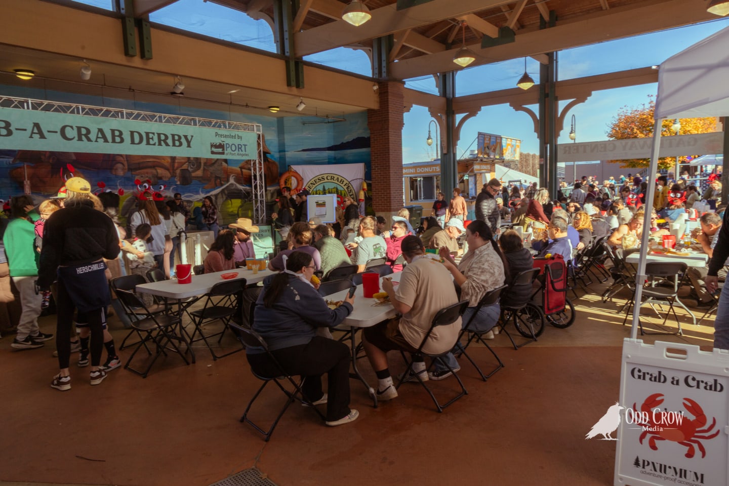 Crowded pavilion tables at the Dungeness Crab Festival with the crab derby sign at the edge of the frame