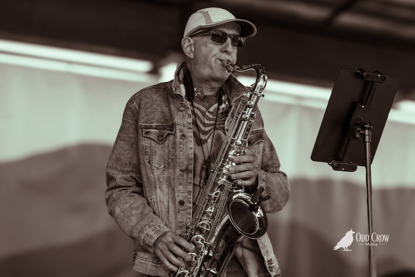 Saxophone player in a denim jacket and cap playing at the Crabfest stage, black and white edit