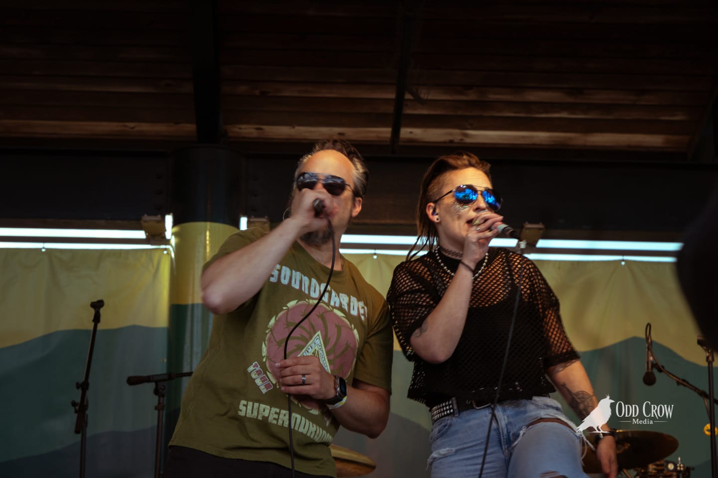 Male vocalist in a Soundgarden shirt and a female vocalist in blue mirrored sunglasses sharing the front of the stage