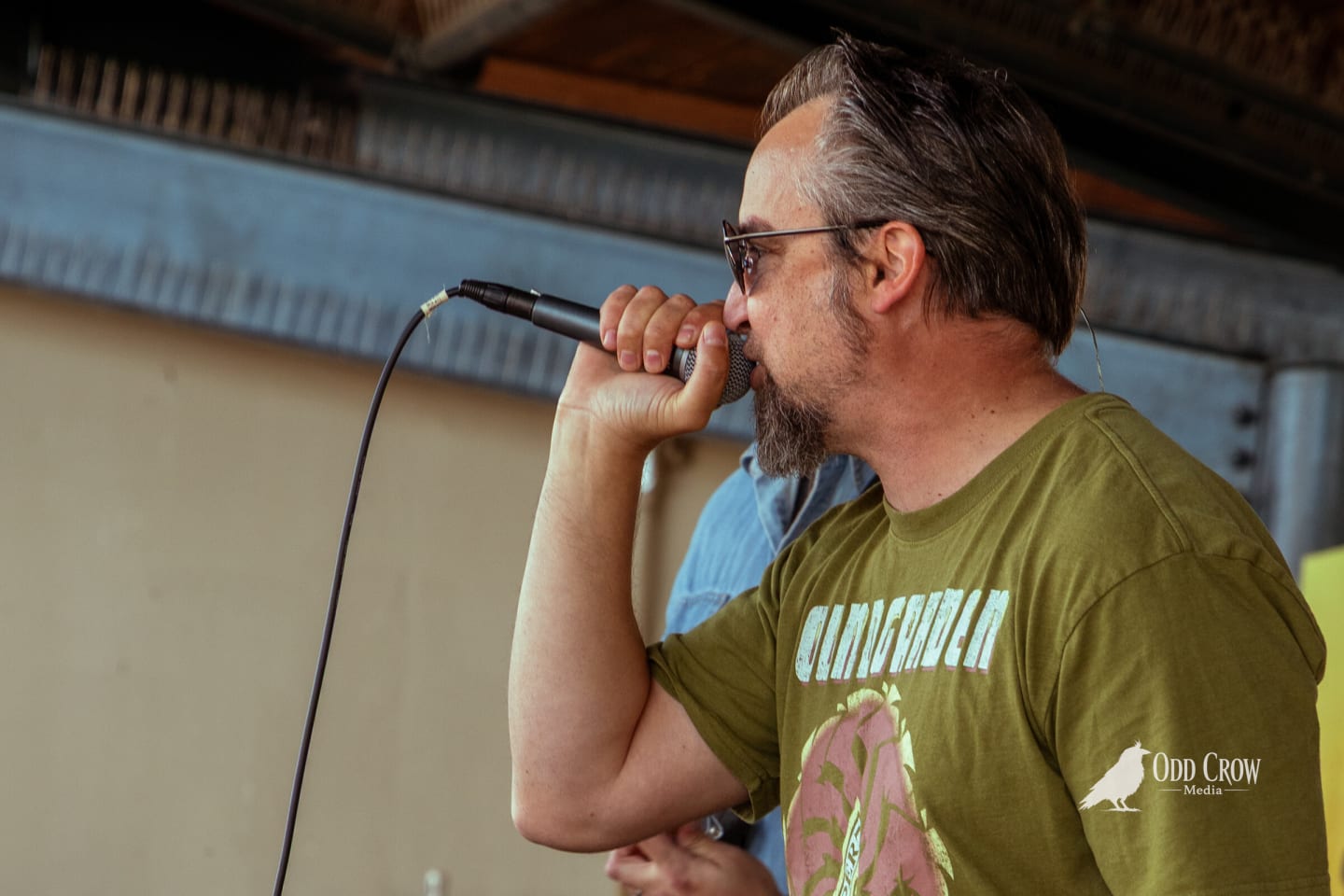 Male vocalist in an olive band shirt singing into a handheld microphone in profile