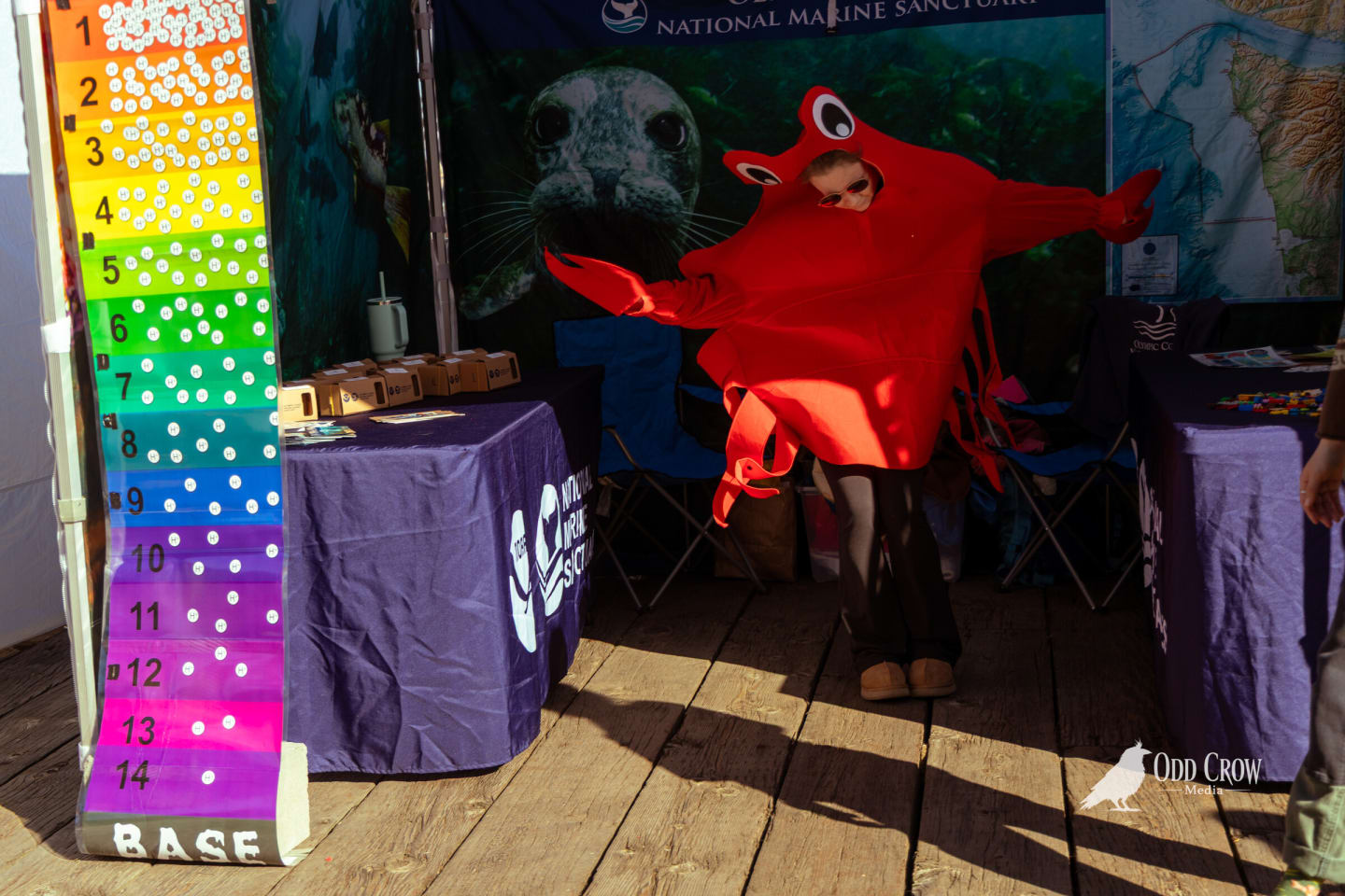 Person in a bright red crab costume at the National Marine Sanctuary booth, ocean depth chart beside them